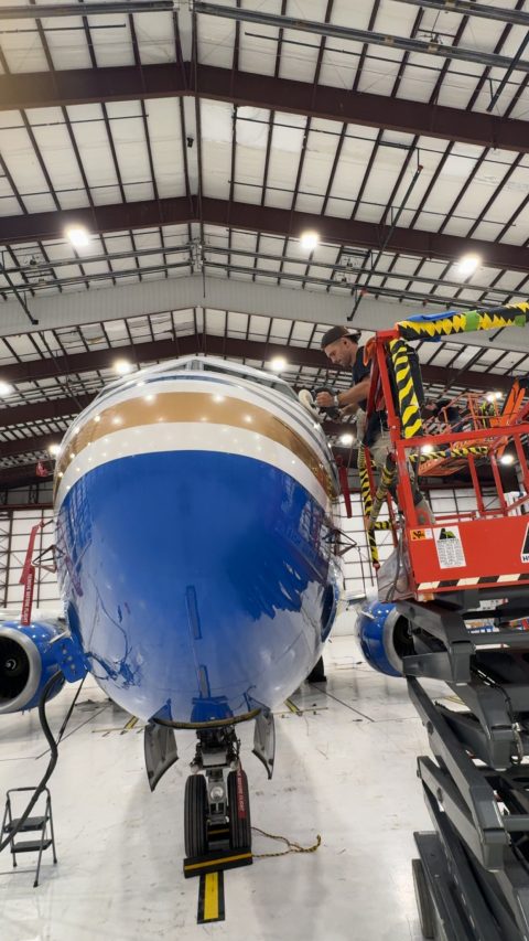 Detailer working from a lift platform, polishing the nose of an airliner inside a hangar