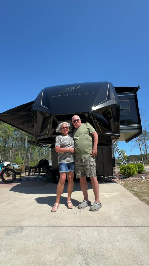 Customers standing in front of their ceramic-coated Brinkley fifth wheel at their campsite