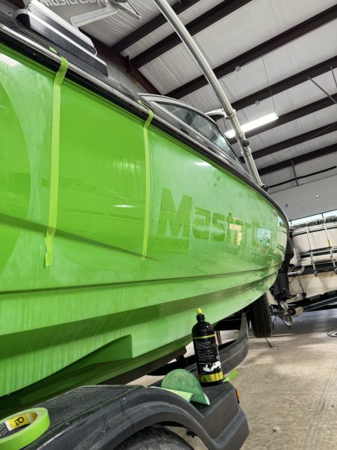 Lime green MasterCraft hull taped off mid machine polish, with compound and a cutting pad alongside