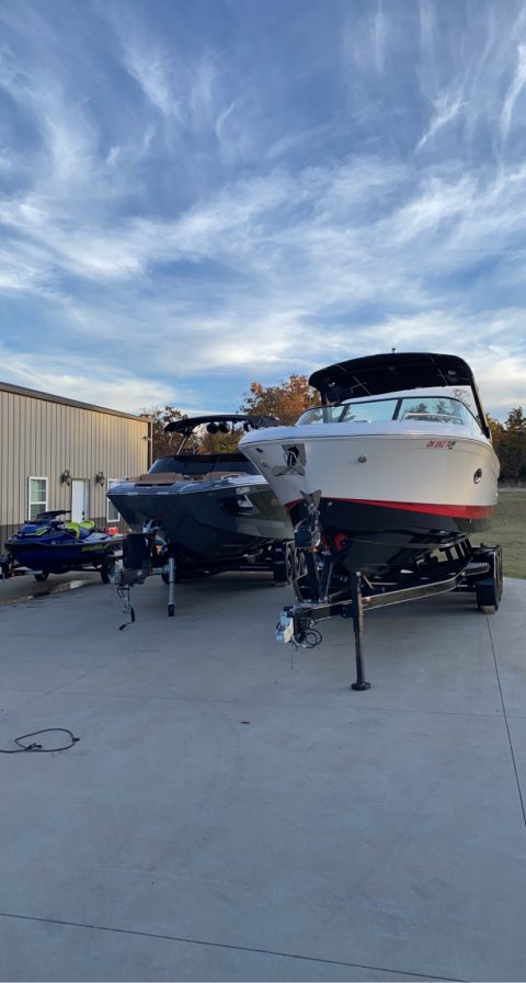 Two detailed wake boats and a jet ski lined up on their trailers at golden hour