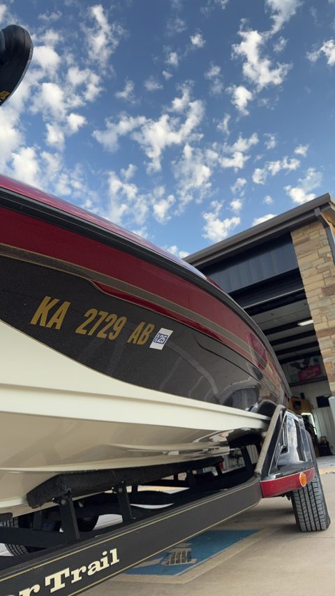 Low angle along the red and gold flake side of a detailed bass boat against a cloudy sky
