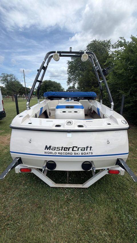 Stern of a blue and white MasterCraft ski boat parked on grass after a wash