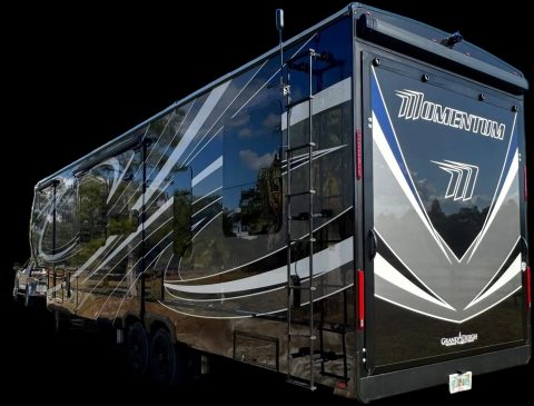 Black Grand Design Momentum fifth wheel finished to a mirror gloss, the sky and treeline reflecting off its side