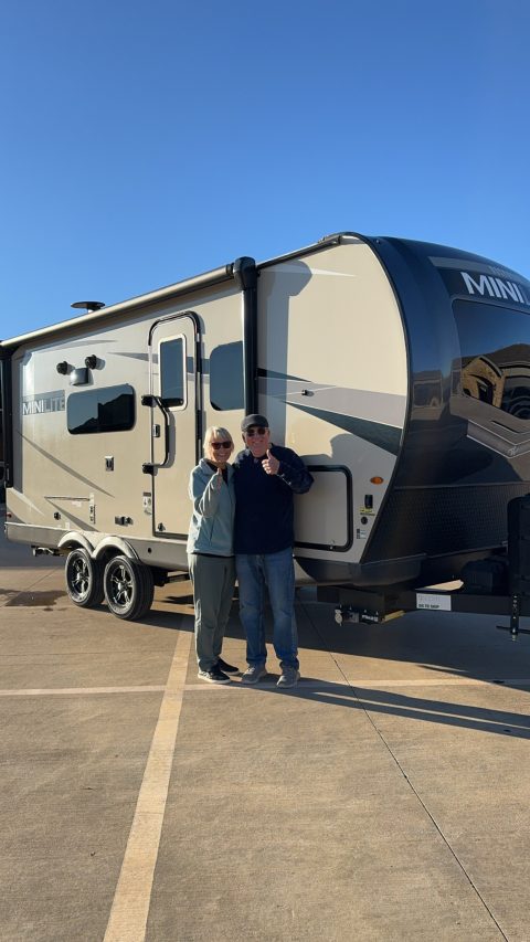 Happy customers giving a thumbs up beside their travel trailer